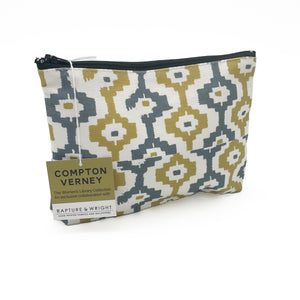 A cosmetic bag with a grey and yellow geometric pattern on a white background. The zip across the top is black and the bag has a brown and white Compton Verney swing tag on it.