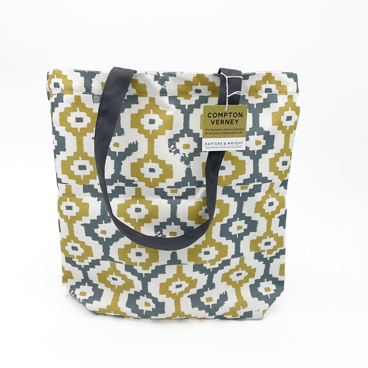 A tote bag featuring a grey and yellow geometric pattern with grey handles. The bag has a brown and white Compton Verney swing ticket on it.