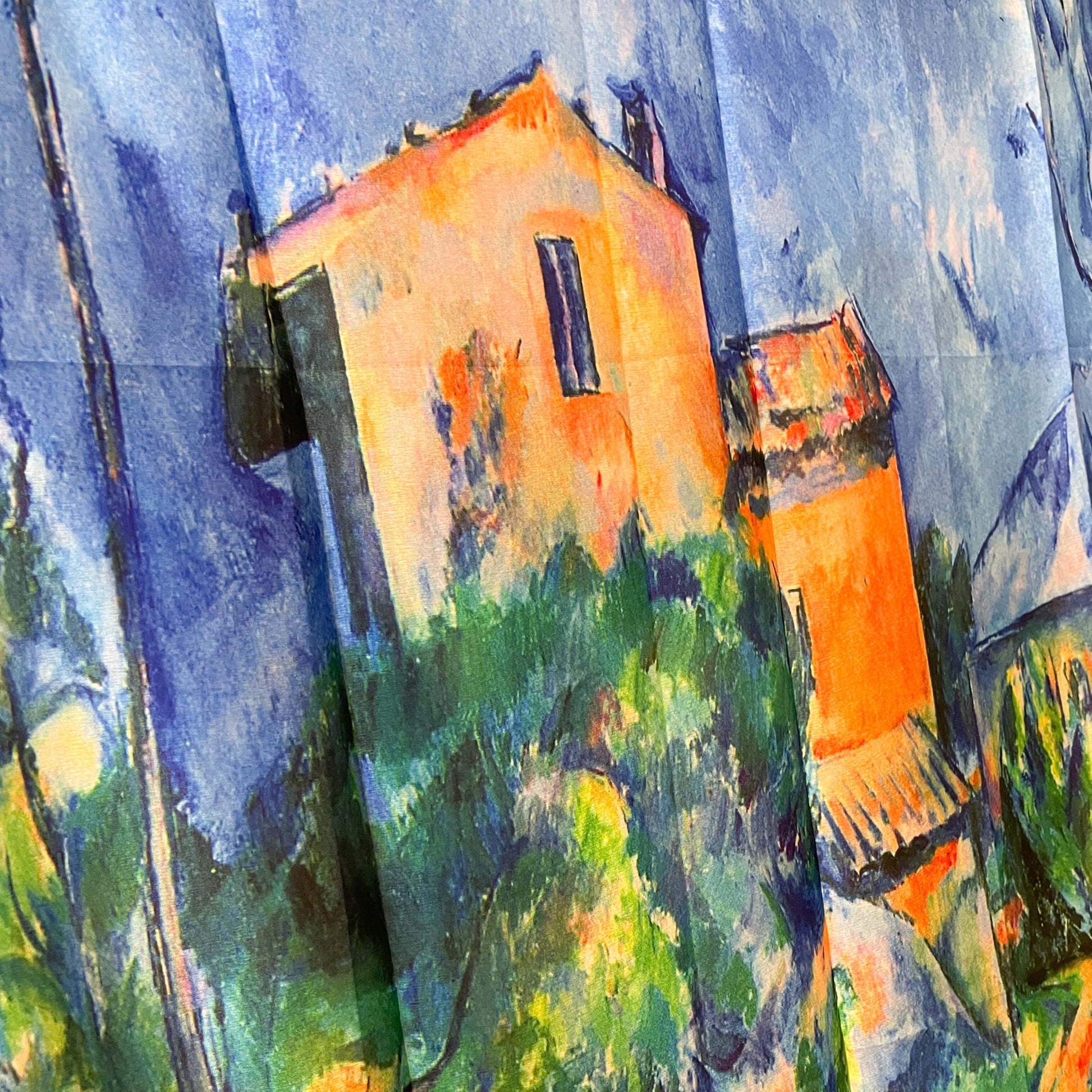 A close up detail of the Cezanne silk scarf showing a French house shaded in orange with green foliage around.