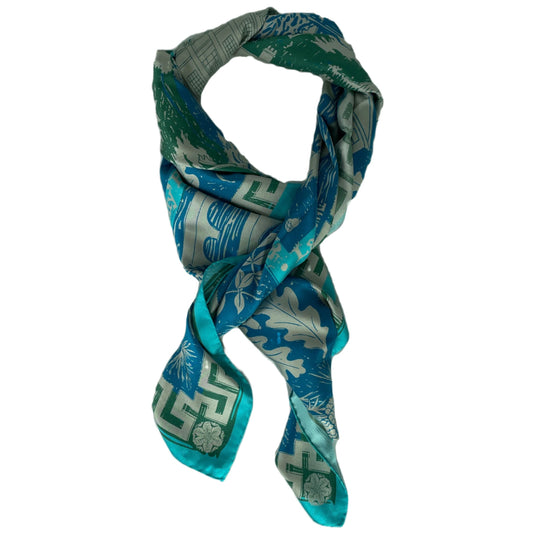 A silk scarf laid out in a knot shape with shades of light blue, dark blue, green and grey from the geometric design.